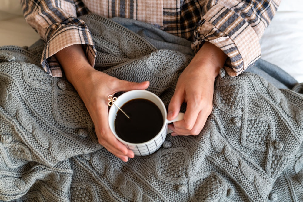 Steaming mug of tea, an open book and a wool blanket on a windowsill, rain on the glass outside
